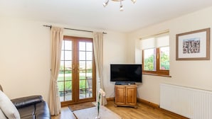 A living room with a leather sofa, a wooden coffee table, a television on a wooden stand, and a large window with curtains. - Wild Duck Lodge (Ormskirk)