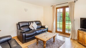 A living room with a black leather sofa, a wooden coffee table, and a television on a wooden cabinet. - Wild Duck Lodge (Ormskirk)