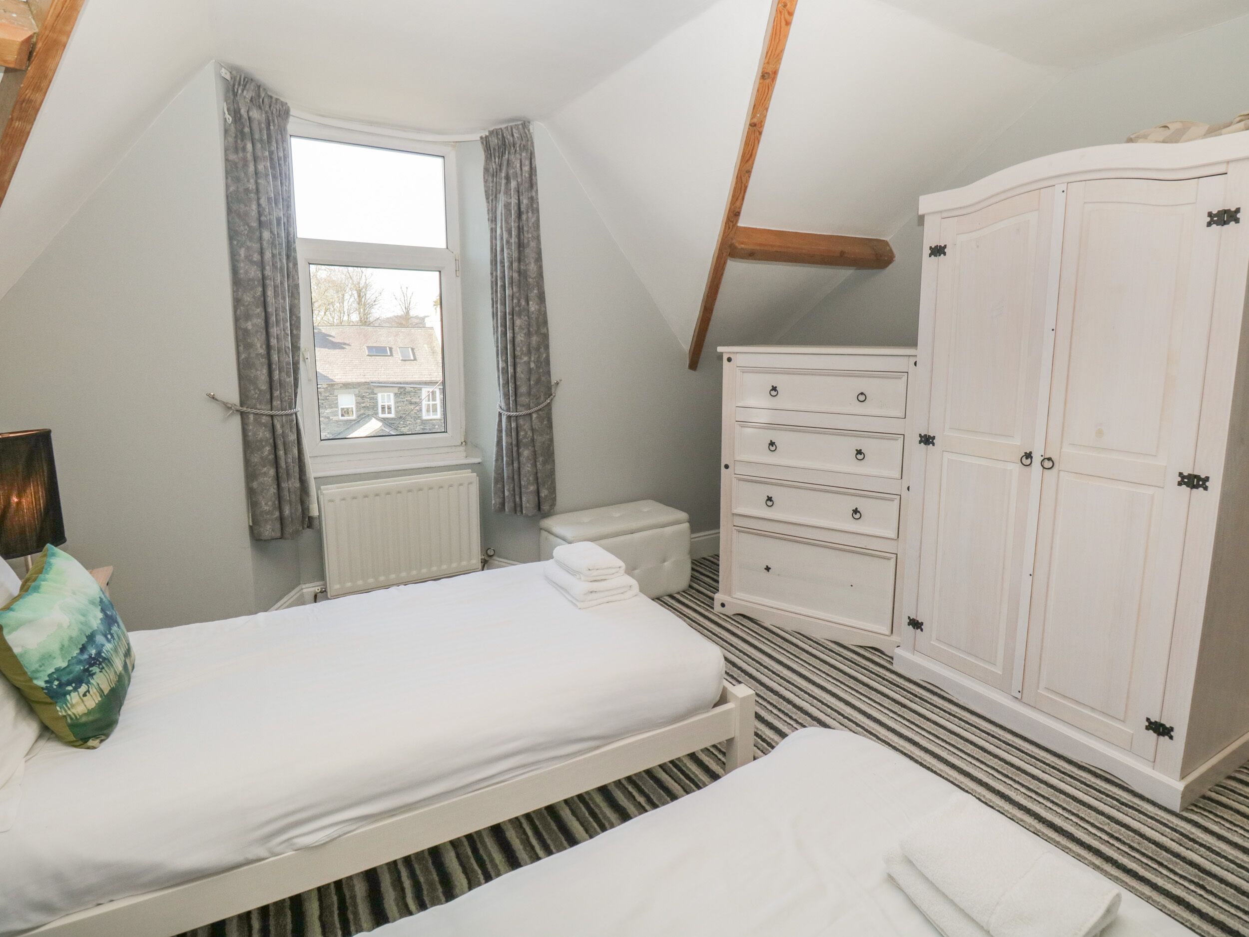 A bedroom with a bed, a dresser, a radiator, and a window with curtains.