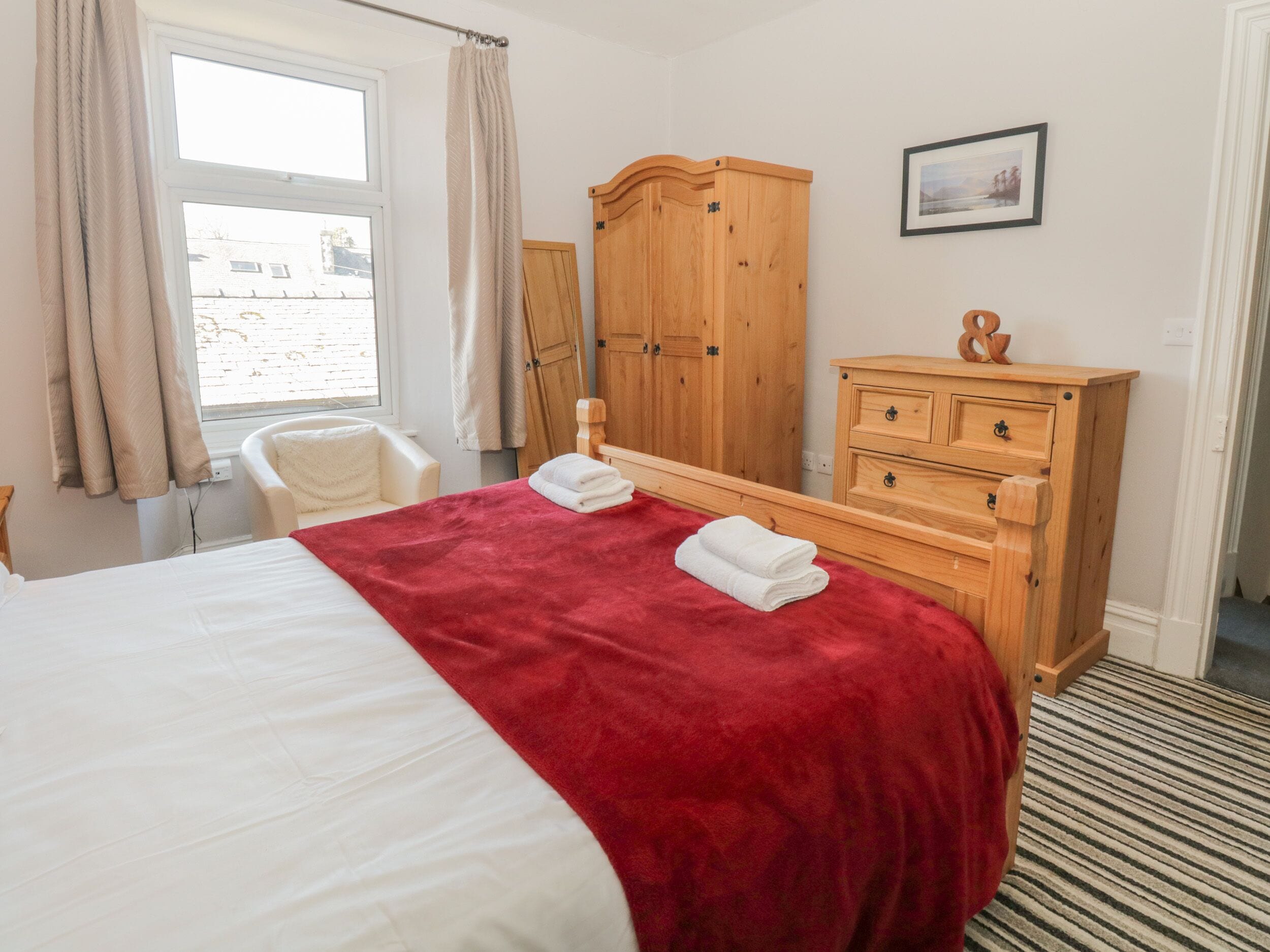A hotel room with a bed, a wooden wardrobe, a chair, and a window with curtains.