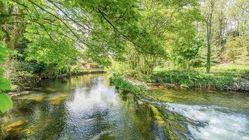 A river flowing through a forested area with a small building in the background.