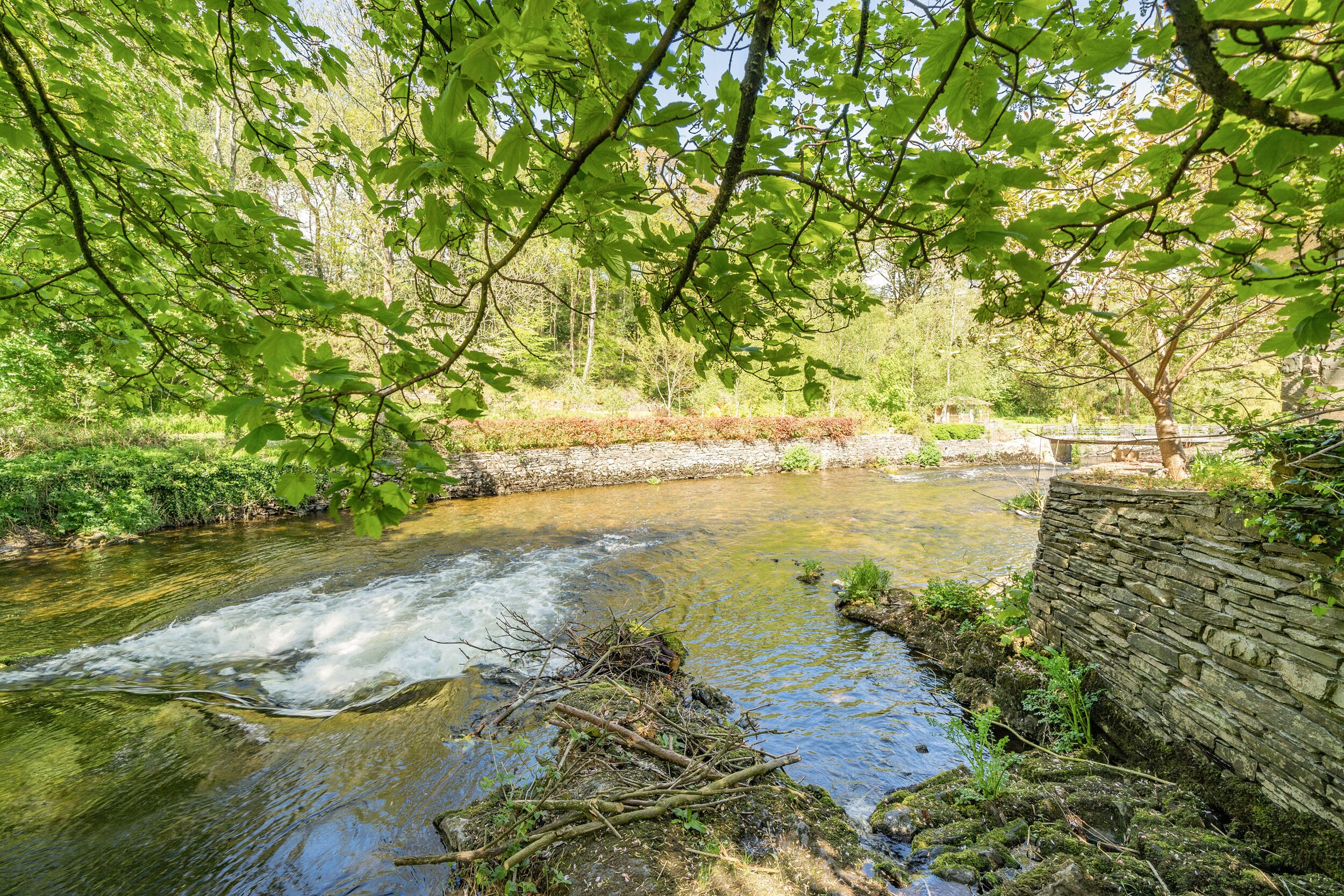 Un río que serpentea por un área boscosa con un muro de piedra a un lado.