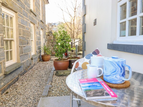 Ein kleiner Außenbereich mit Tisch, Stühlen, einem Blumentopf und einem Fenster.
