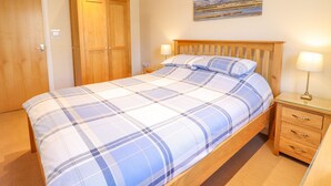 A bedroom with a bed, wooden wardrobe, bedside table, and a painting on the wall. - Taliesin (Porthmadog)