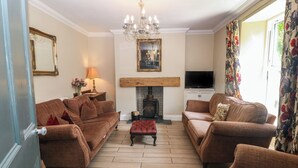 A living room with two sofas, a fireplace, a television, and a chandelier. - Trevor Cottage (Llandudno)