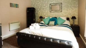 A neatly arranged bedroom with a large bed, two bedside tables, a wall-mounted heater, and a framed picture. - Westgate Retreat (Hunstanton)