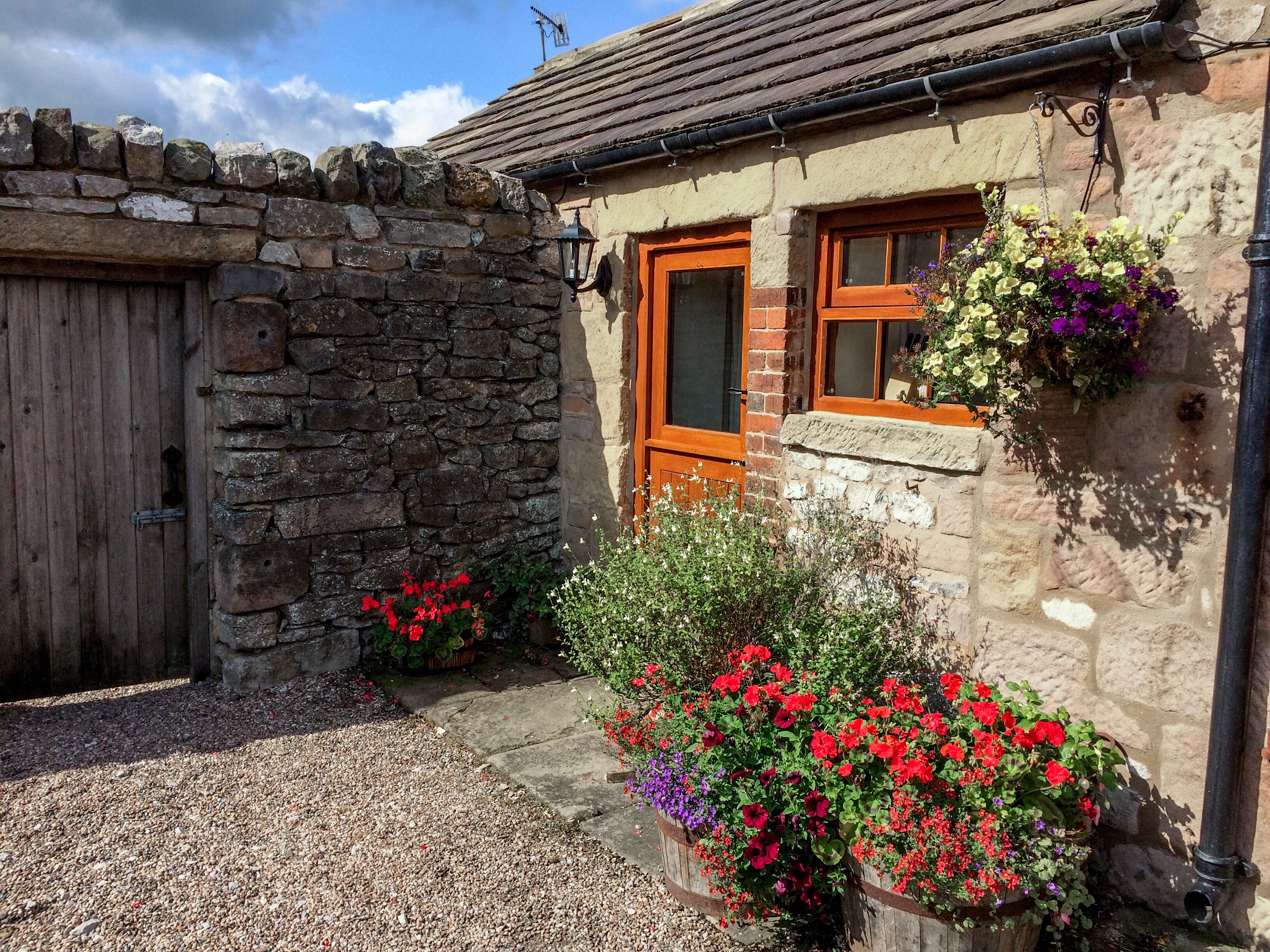 A stone building with a wooden door and windows, surrounded by gravel and flower beds.