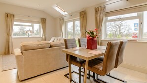 A modern living room with a sofa, dining table, and chairs. There are windows with curtains, a skylight, and a view of the outdoors. - Sunnyside Shreyas (Blackburn)