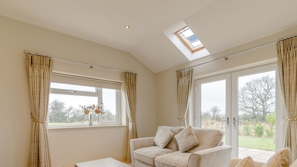 A spacious living room with a high ceiling, a skylight, a sofa set, a coffee table, and large windows offering a view of the outdoors. - Sunnyside Shreyas (Blackburn)