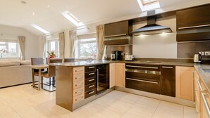 A modern kitchen with a central island, built-in appliances, and a dining area with a sofa and table. - Sunnyside Shreyas (Blackburn)
