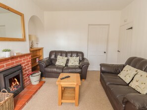 A living room with a fireplace, two leather sofas, a wooden coffee table, and a white door. - 1 Organsdale Cottages (Tarporley)