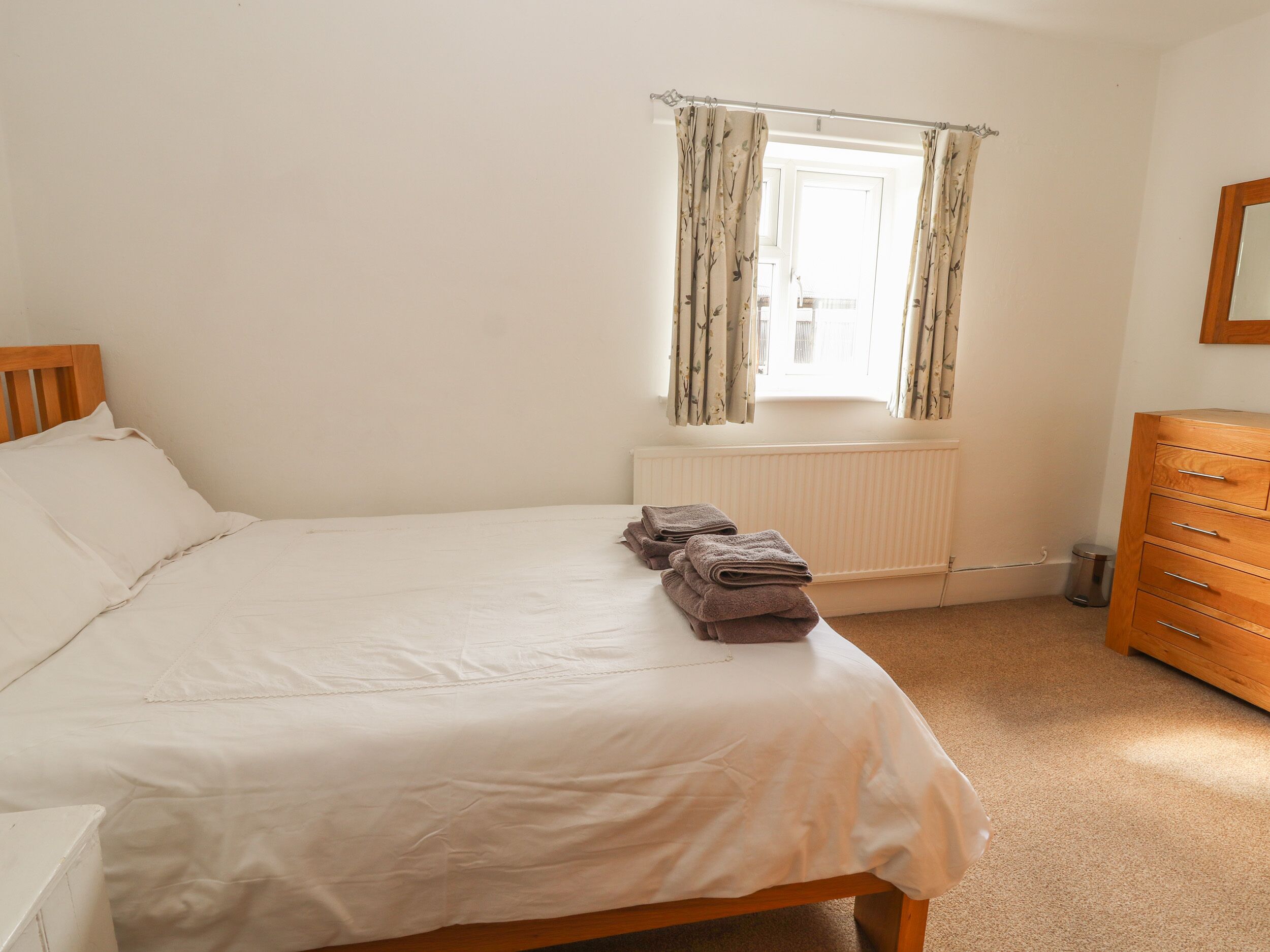 A bedroom with a bed, a radiator, a window with curtains, and a wooden dresser.