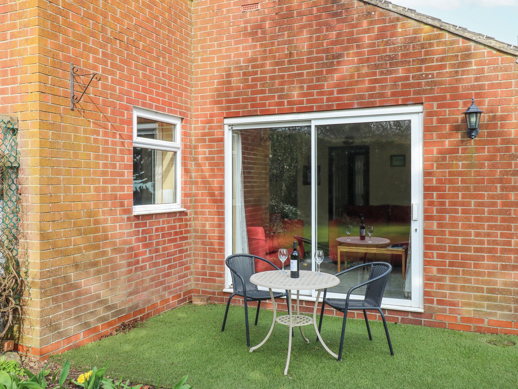 Une maison en briques dotée d’un patio comprenant une table ronde et deux chaises, une fenêtre et une porte-fenêtre coulissante.
