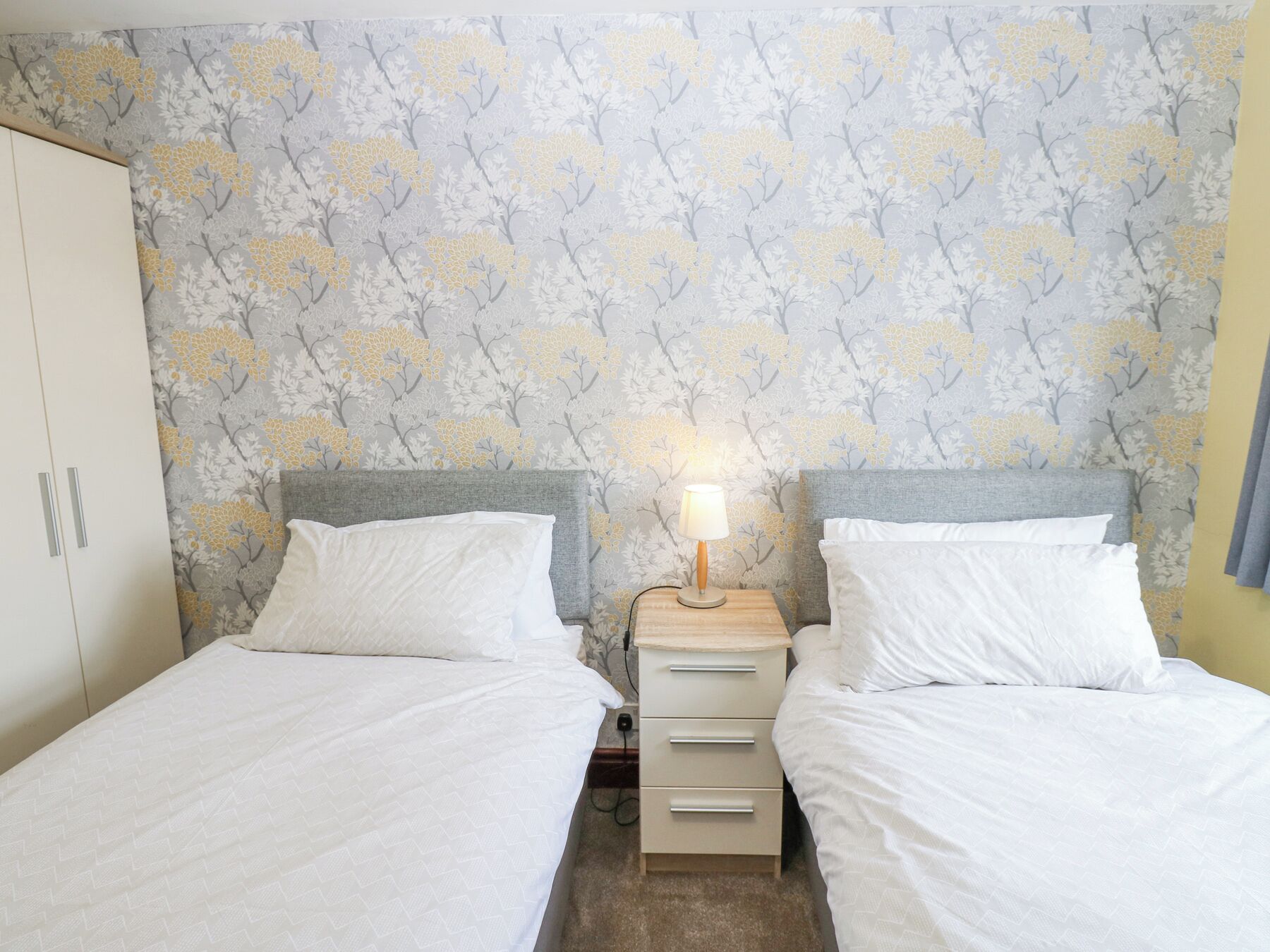 A bedroom with two beds, a wardrobe, and a nightstand with a lamp.