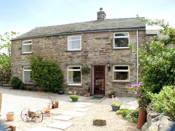 A stone house with a front door, windows, and a small garden with potted plants. - Maryend (Hawes)