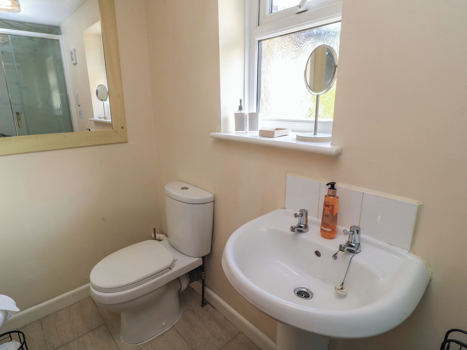 A bathroom with a toilet, sink, mirror, and window.