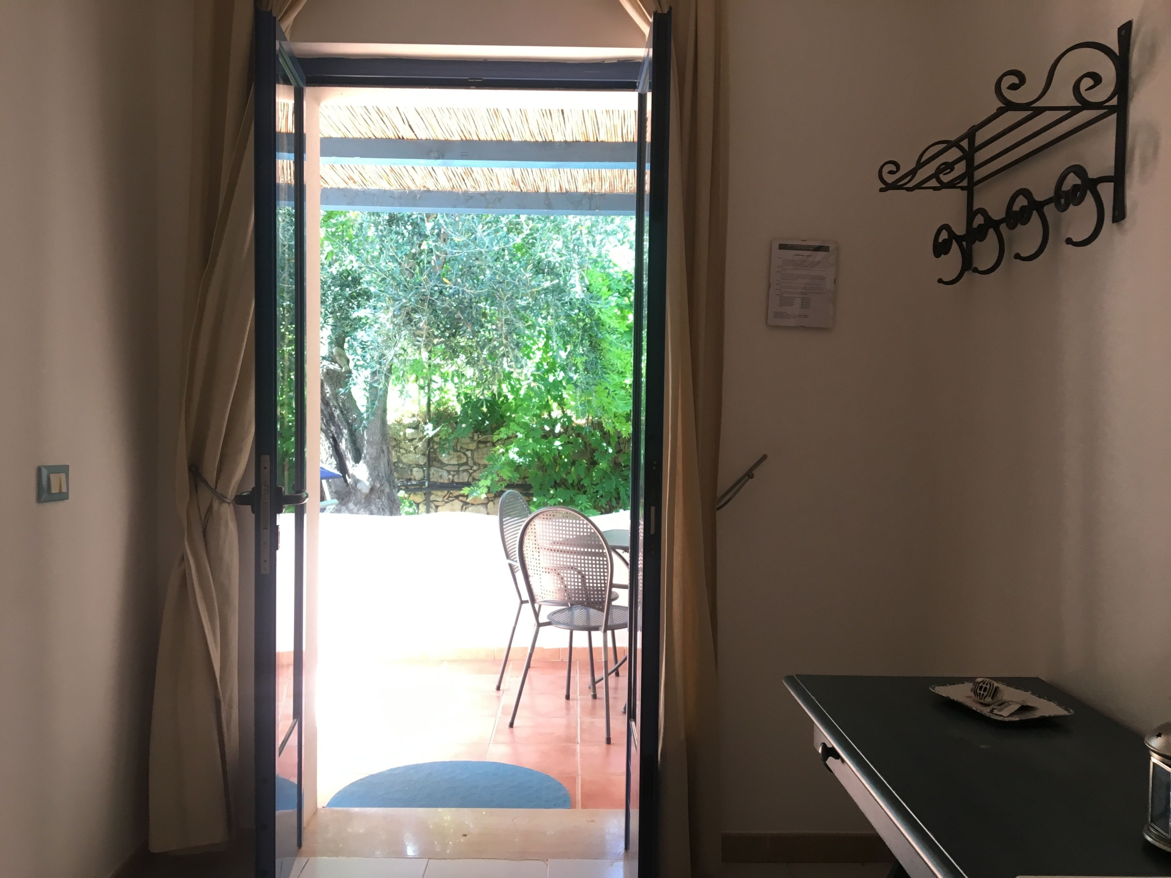 A doorway leading to an outdoor patio with a chair and table, a wall-mounted decorative item, and a small table with a lamp.