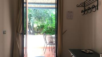 A doorway leading to an outdoor patio with a chair and table, a wall-mounted decorative item, and a small table with a lamp.
