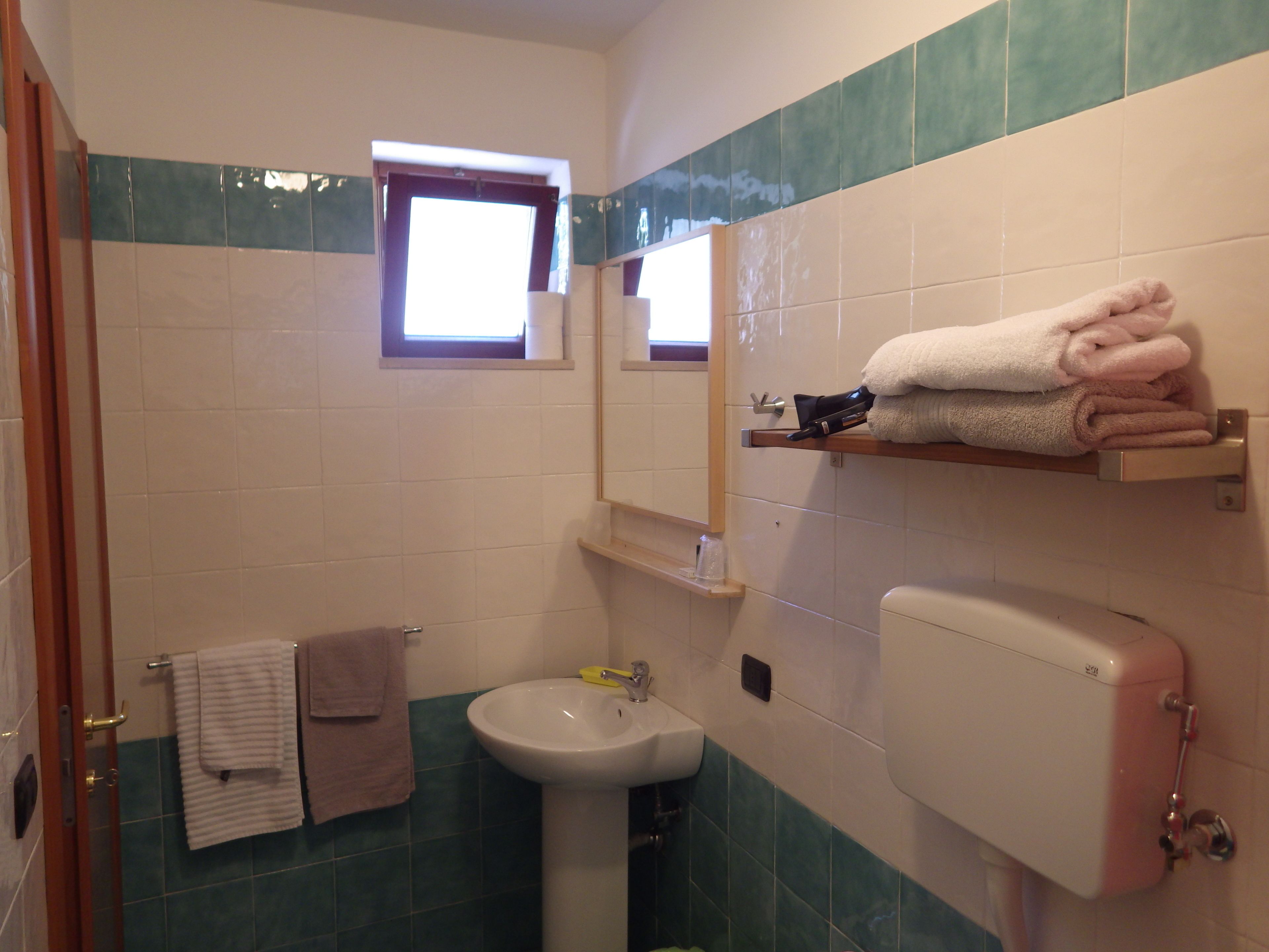 A bathroom with a sink, toilet, and a window. There are towels on a rack and a mirror above the sink.