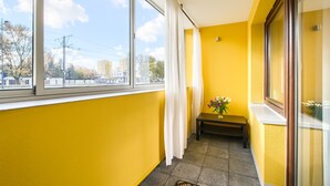 A narrow corridor with yellow walls, a bench, a vase with flowers, and large windows offering a view of buildings and trees. - Roztocka Loft Apartment (Warsaw)