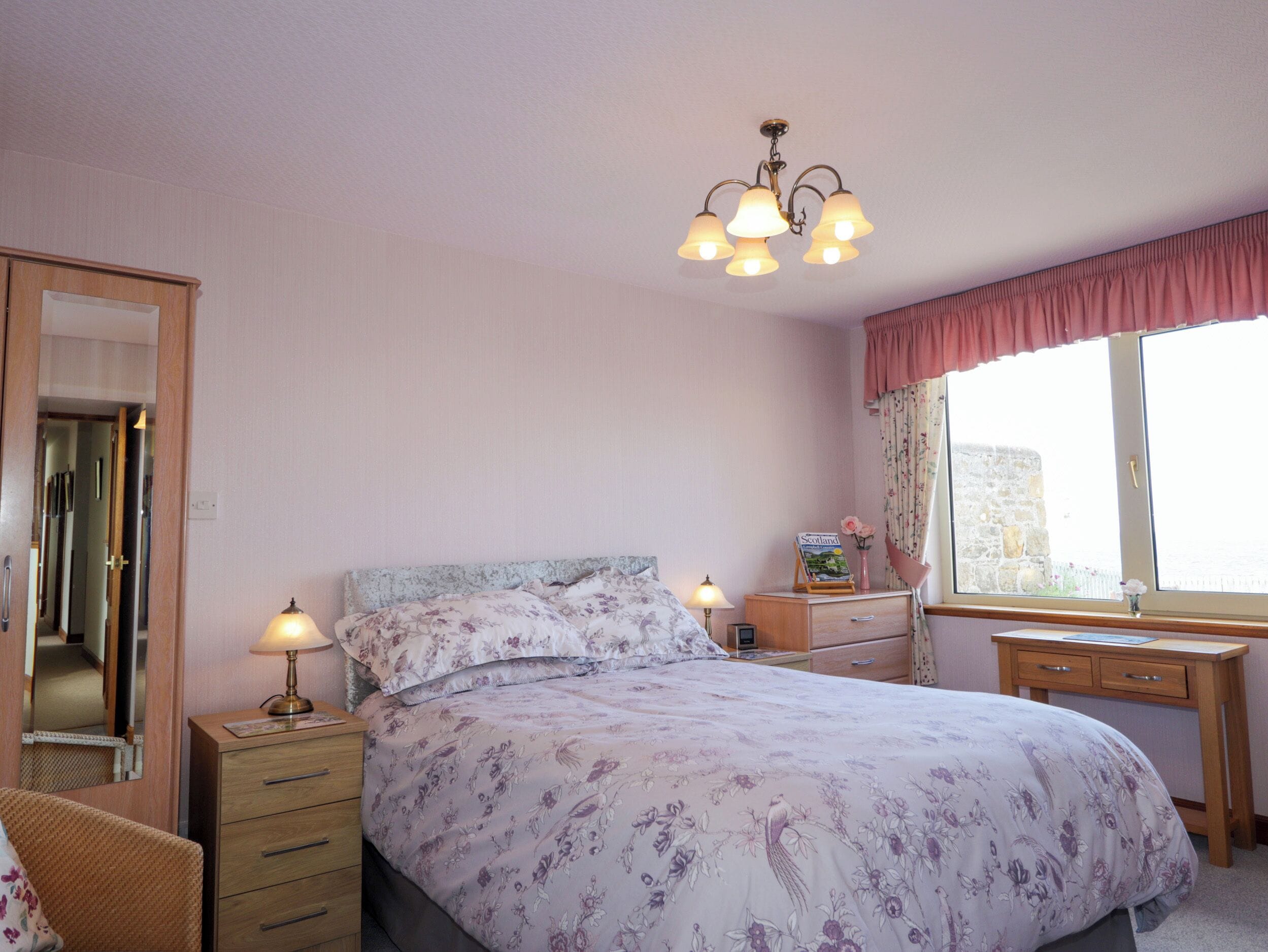 A bedroom with a bed, bedside tables, a dresser, a window with curtains, and a mirror.