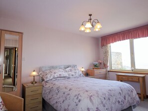A bedroom with a bed, bedside tables, a dresser, a window with curtains, and a mirror.