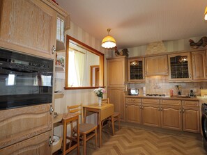 A kitchen with wooden cabinets, a built-in oven, a dining table with chairs, and a hanging light fixture.