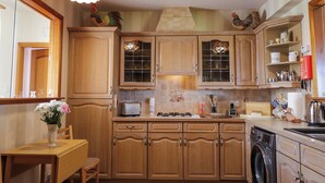 A kitchen with wooden cabinets, a dining table with chairs, a washing machine, and hanging light fixtures. - Braehead Croft (Buckie)