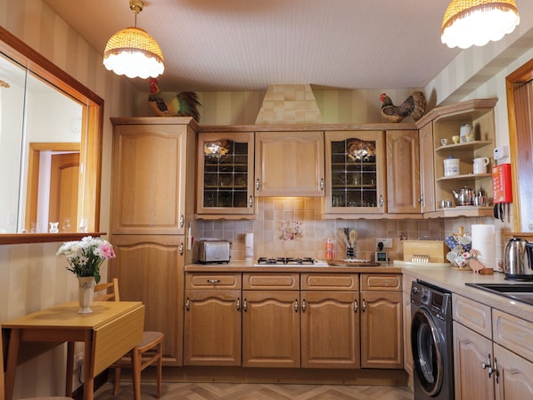A kitchen with wooden cabinets, a dining table with chairs, a washing machine, and hanging light fixtures.