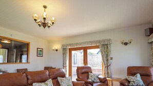 A living room with leather sofas, a chandelier, and a view to the outside. - Braehead Croft (Buckie)