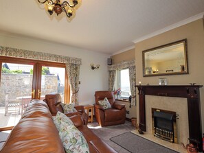 A living room with a fireplace, leather sofas, a dining area, and a view through the glass doors.