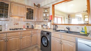 A kitchen with wooden cabinets, a washing machine, a sink, and a large mirror. - Braehead Croft (Buckie)