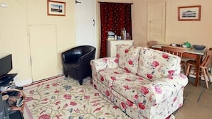 Un salon avec un canapé à motifs floraux, un fauteuil noir, une table à manger avec des chaises et un téléviseur.