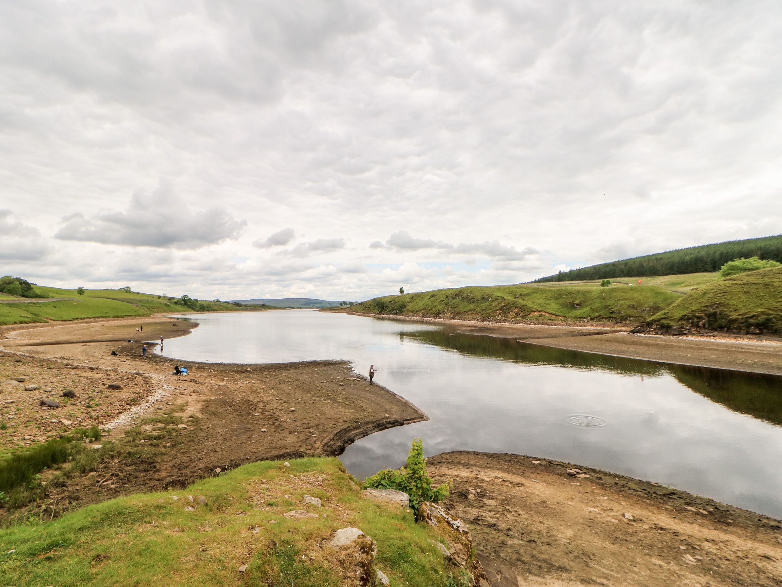 A river with a bridge, grassy banks, and a cloudy sky.