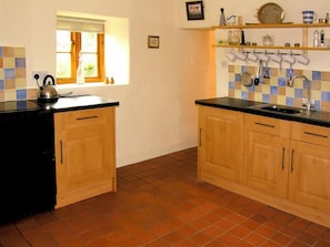 A kitchen with wooden cabinets, a black countertop, a window, and a tiled backsplash. - Pen y Parc (Rhyl)
