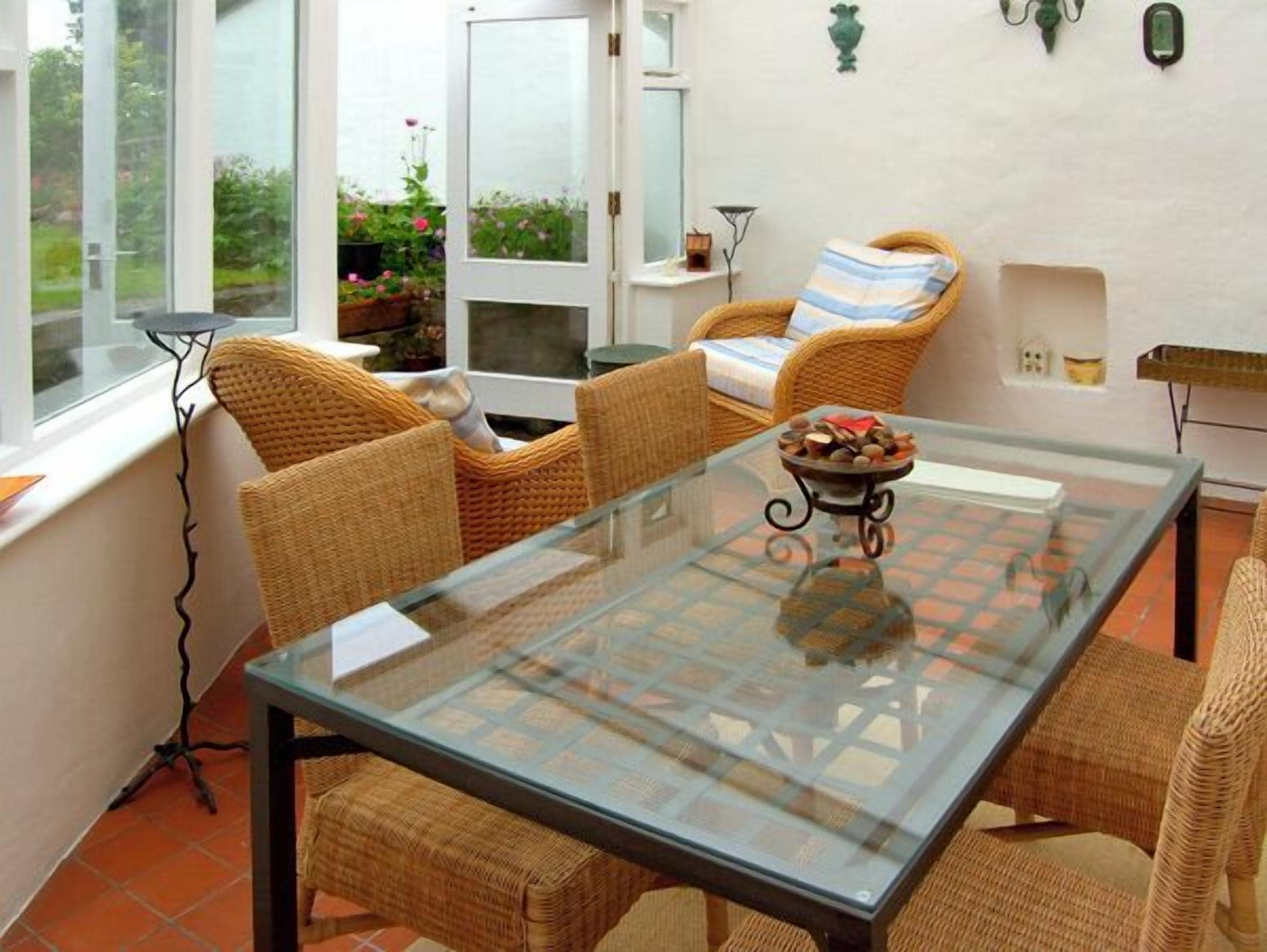A glass-top table with wicker chairs in a sunlit room with large windows.