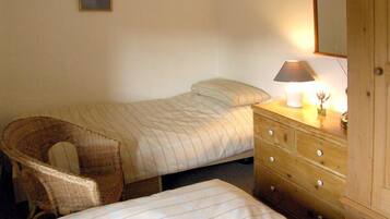 A bedroom with two beds, a wooden dresser, a chair, and a bedside lamp.