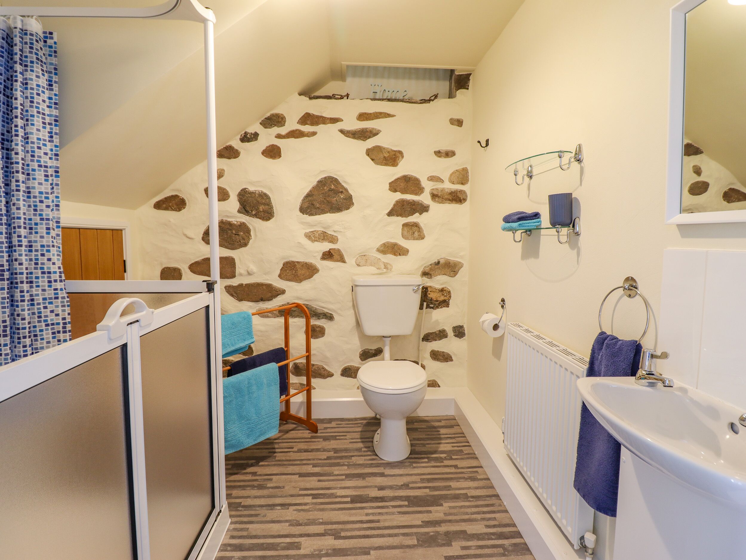 A bathroom with a stone wall, a toilet, a bathtub, and a shower area.