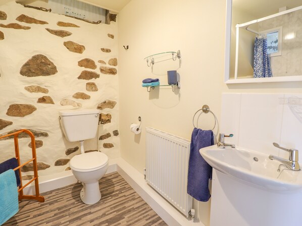 Un baño con pared de piedra, inodoro, bañera, lavamanos y perchero para toallas.