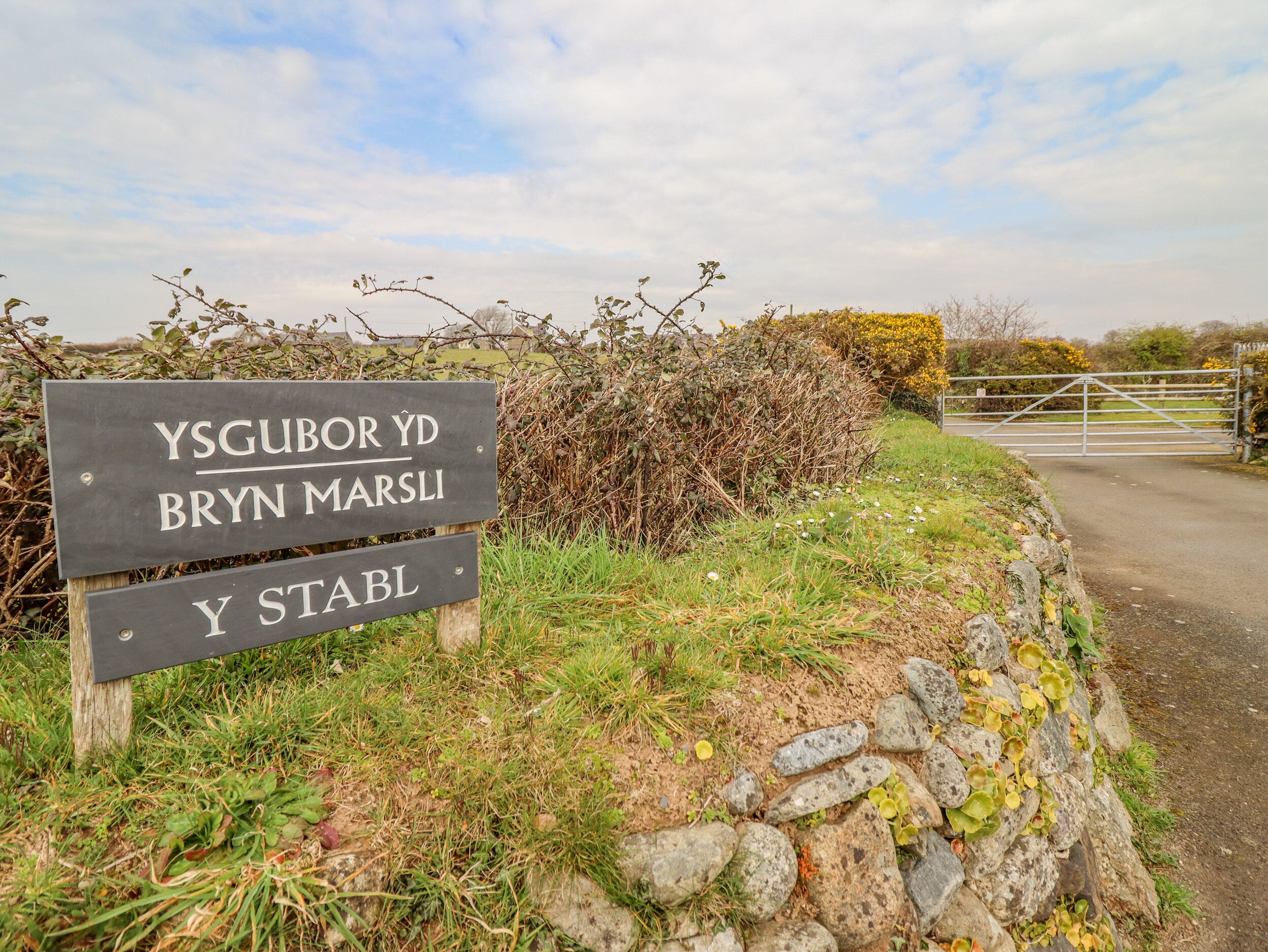 A sign with text in a non-English language, a stone wall, and a metal gate.