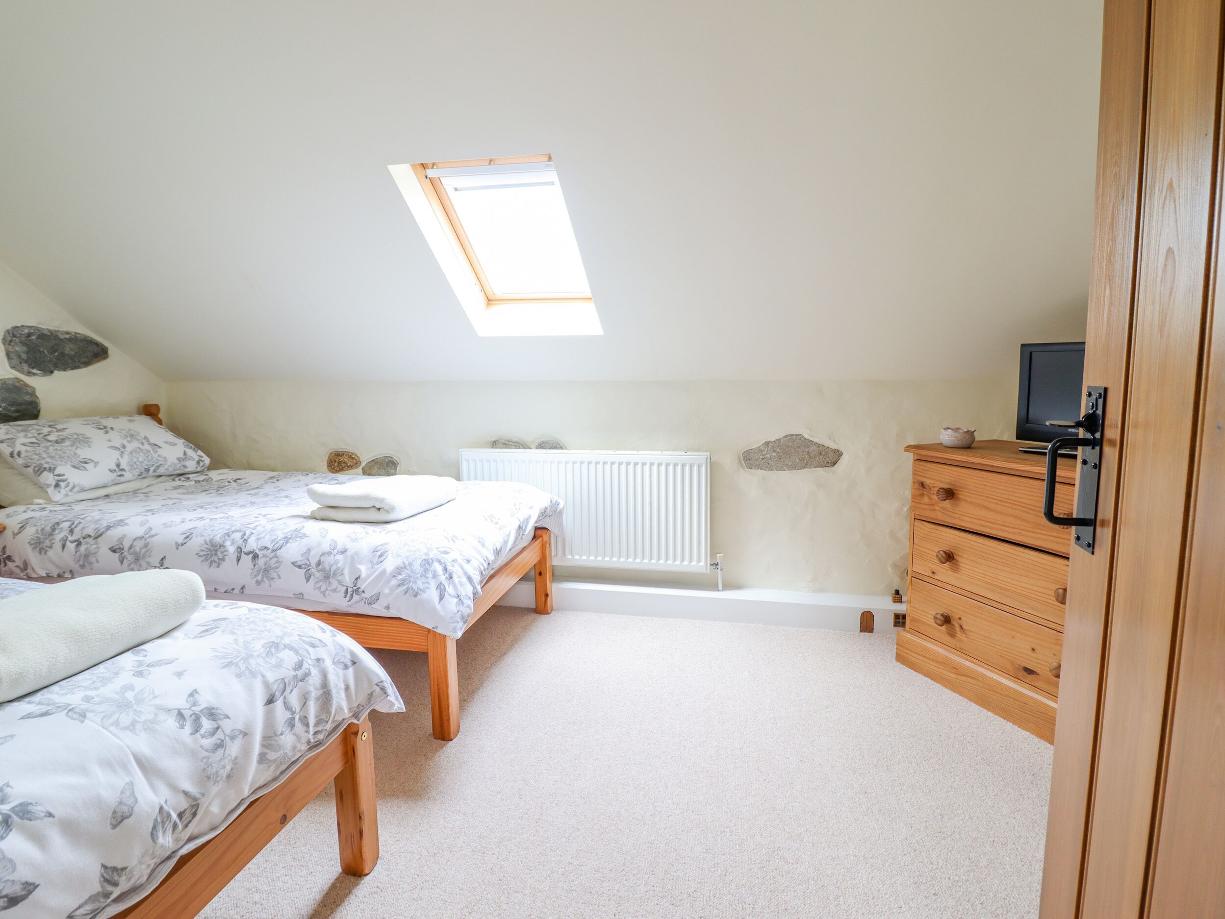 A bedroom with two beds, a wooden dresser, a radiator, and a skylight.