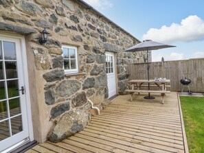 Un edificio de piedra con terraza de madera, una mesa de picnic y una parrilla.