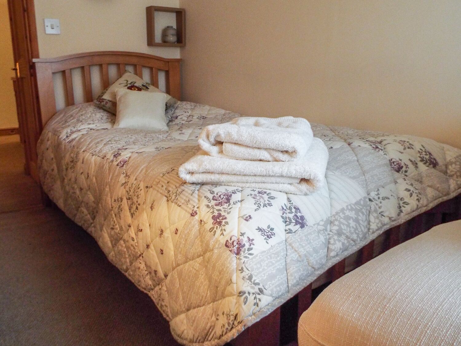 A neatly made bed with a floral-patterned bedspread and a stack of folded towels.