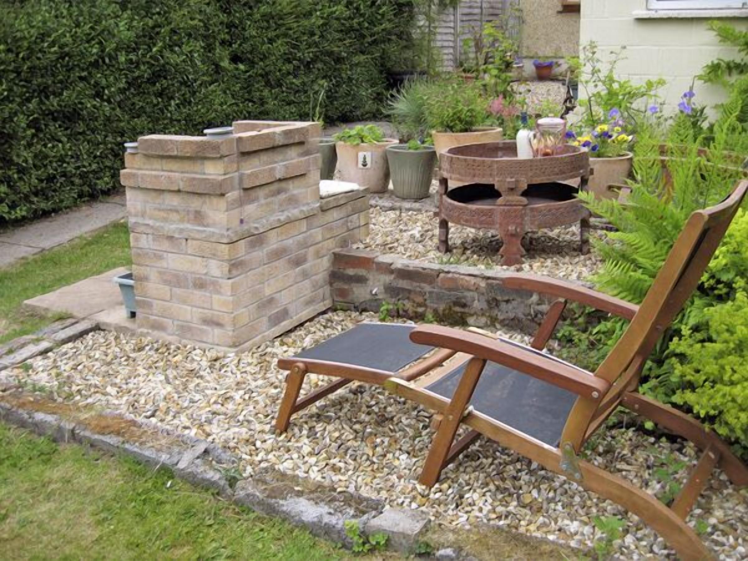 Un jardin agrémenté d’un foyer en pierre, d’un banc en bois et de diverses plantes en pot.