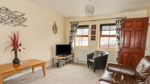 A living room with a brown leather sofa, a wooden coffee table, a TV on a stand, a decorative wall piece, and a door with a curtain. - Prince Cottage (Saltburn-by-the-Sea)