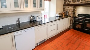 A kitchen with white cabinets, a black countertop, a dishwasher, a stove, and a window with blinds. - Lees Farm (Buxton)
