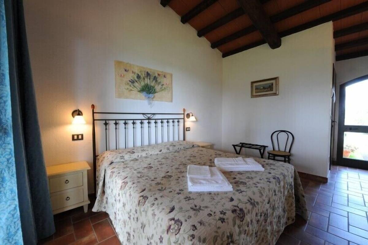 A bedroom with a bed, bedside lamps, a nightstand, a chair, a painting, and a window.