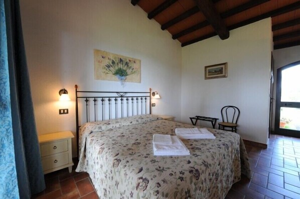 A bedroom with a bed, bedside lamps, a nightstand, a chair, a painting, and a window. - Il Gelsomino (Grosseto)