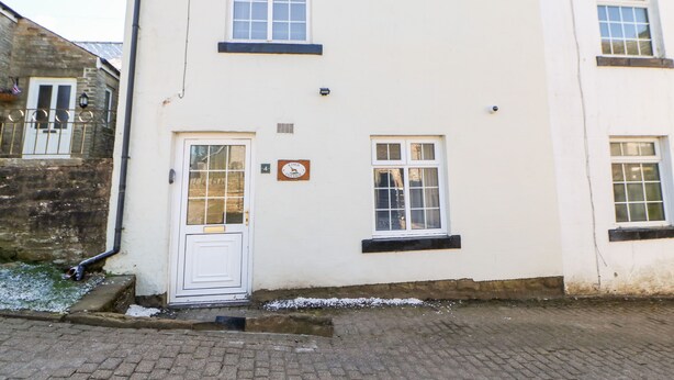 A white building with a white door and two windows. There is a sign on the wall that reads "Kings Cottage." - Kings Cottage (Alston)