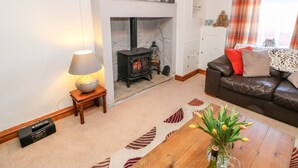 A living room with a fireplace, a sofa, a coffee table with a vase of flowers, and a lamp. - Kings Cottage (Alston)